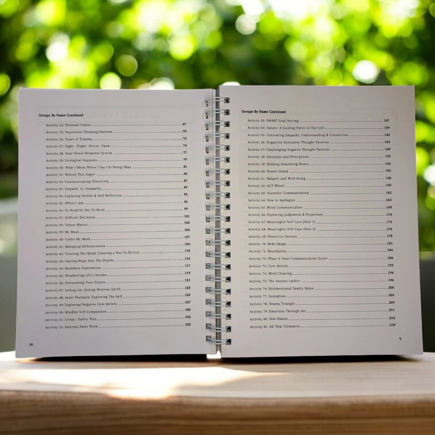 The book open to the table of contents for 100 Group Therapy Activities, showing a list of group therapy activities like "Types of Trauma," "SMART Goal Setting," and "Boundaries."