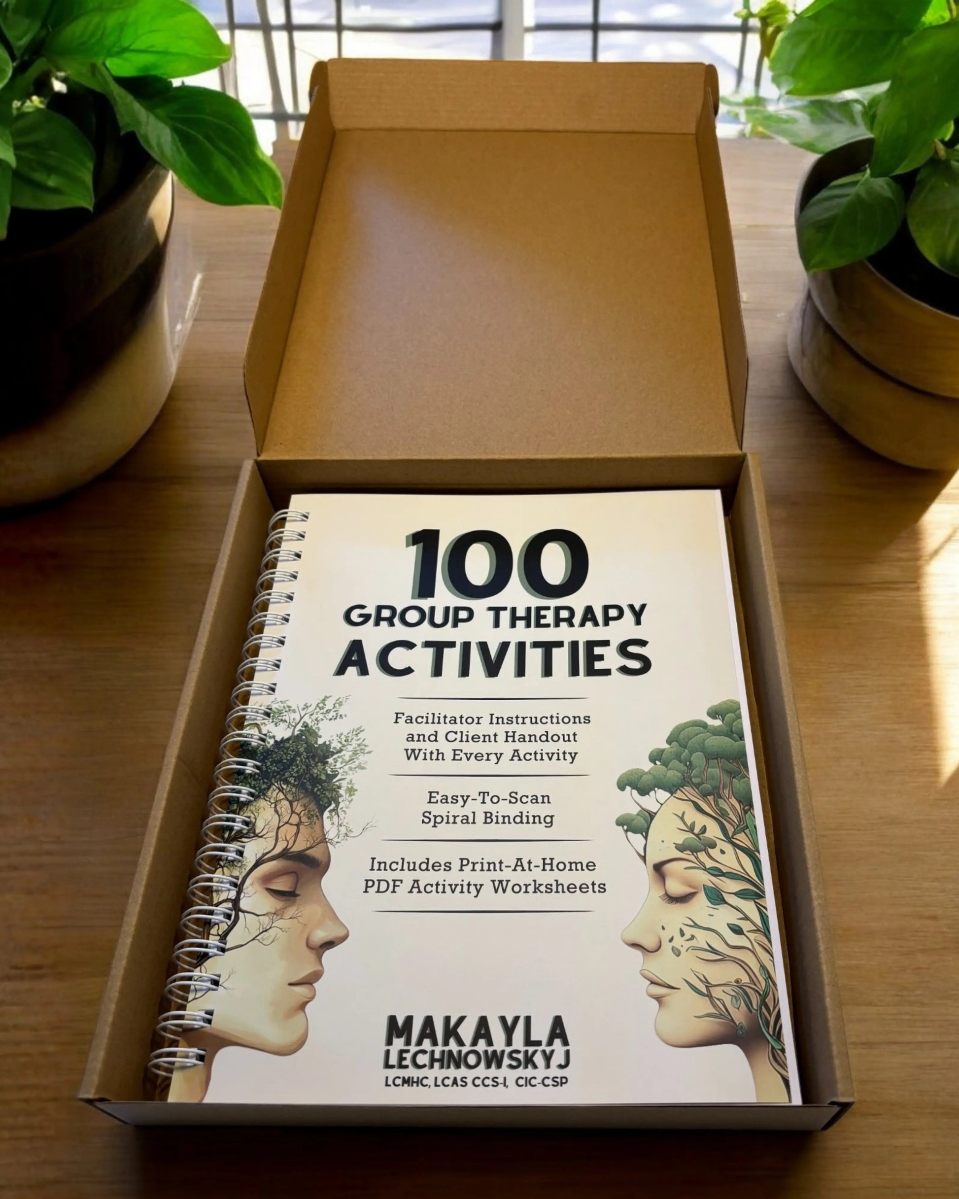 An unboxing view of the 100 Group Therapy Activities book sitting inside its shipping box, surrounded by potted plants.